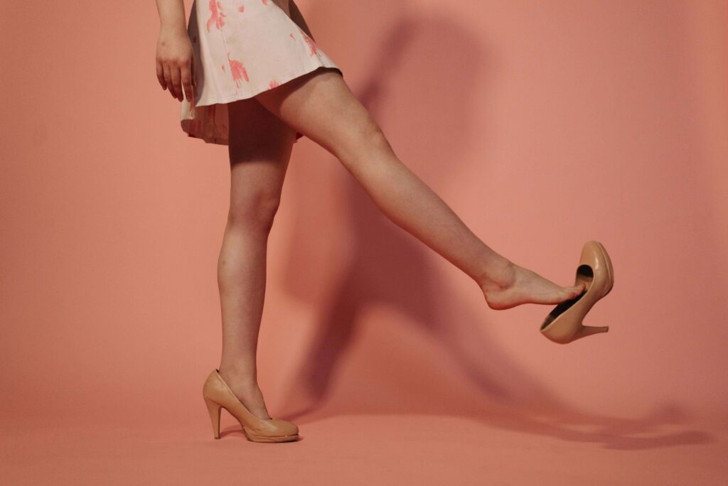 A woman walking and kicking off her beige heel, exposing her foot.